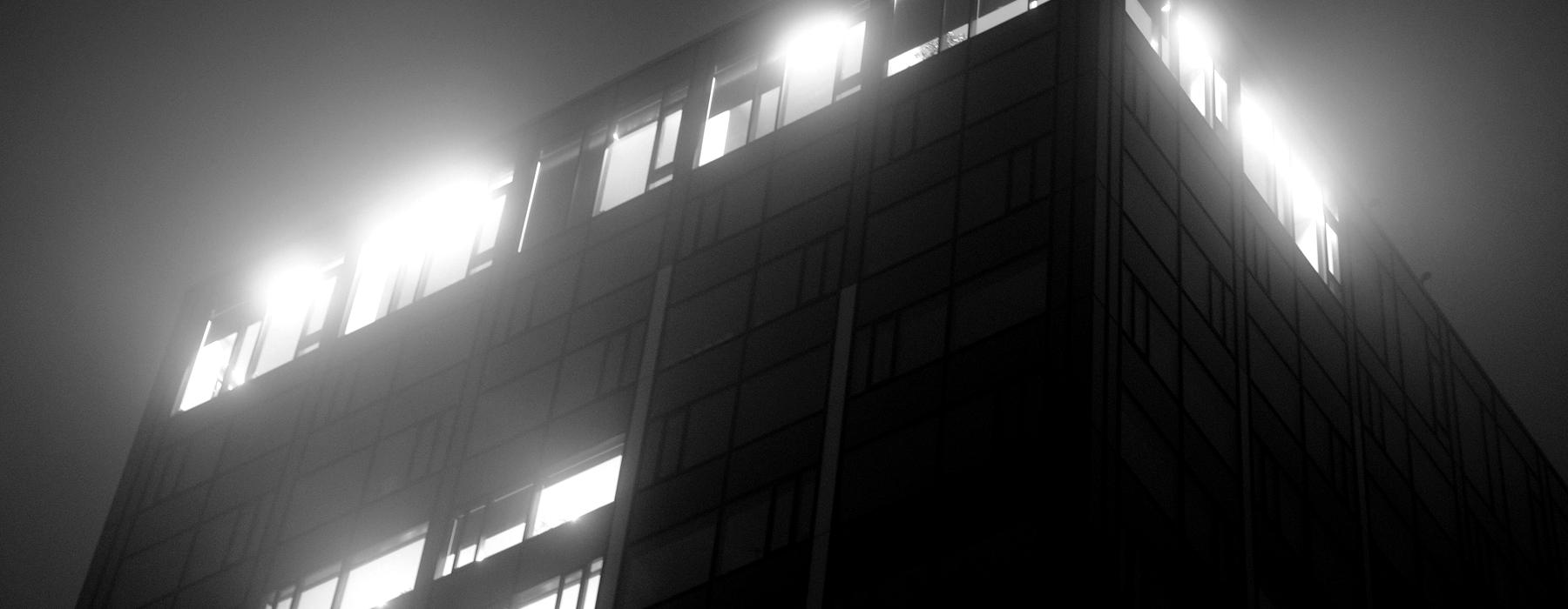 An office building at night with lit windows in fog